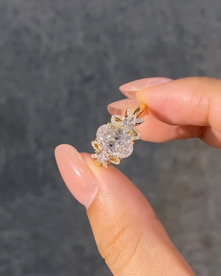 A ring featuring a 2-carat oval lab-grown diamond as the center stone, with a bow-shaped design on the band; graded as D color and VS1 clarity