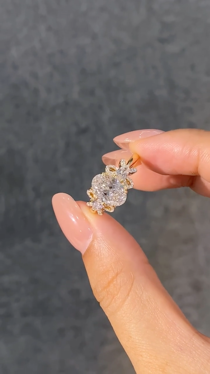 A ring featuring a 2-carat oval lab-grown diamond as the center stone, with a bow-shaped design on the band; graded as D color and VS1 clarity