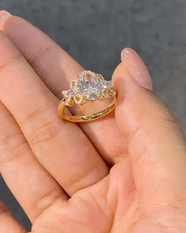 A ring featuring a 2-carat oval lab-grown diamond as the center stone, with a bow-shaped design on the band; graded as D color and VS1 clarity