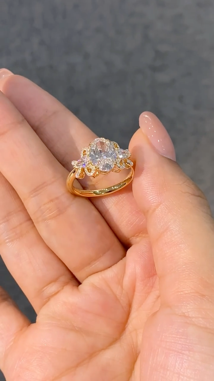 A ring featuring a 2-carat oval lab-grown diamond as the center stone, with a bow-shaped design on the band; graded as D color and VS1 clarity