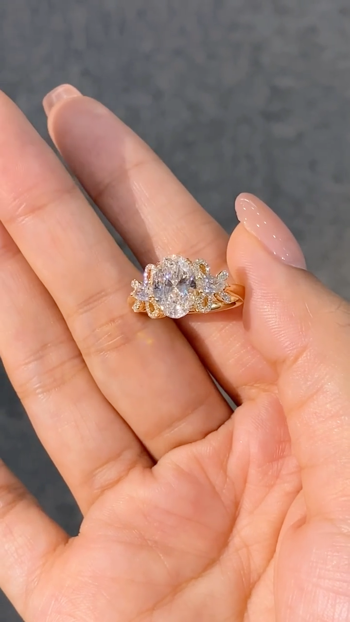 A ring featuring a 2-carat oval lab-grown diamond as the center stone, with a bow-shaped design on the band; graded as D color and VS1 clarity